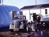 Weapons Release Shop in background. John Baker in white coveralls. Paul Baker with Red hat and Ken Prow barely visible working on car in background.